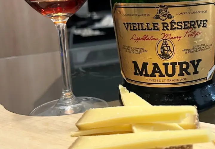 Verre de vin et fromage sur planche en bois, à côté d'une bouteille de Maury. La question est : que boire avec du fromage ?
