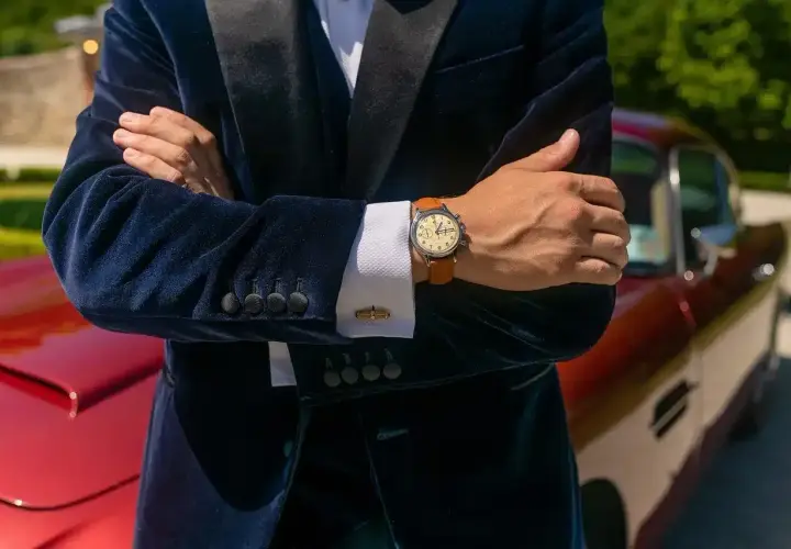 Elegancki mężczyzna w granatowym aksamitnym garniturze i białej koszuli pokazuje, jak nosić zegarek do koszuli. Klasyczny styl.