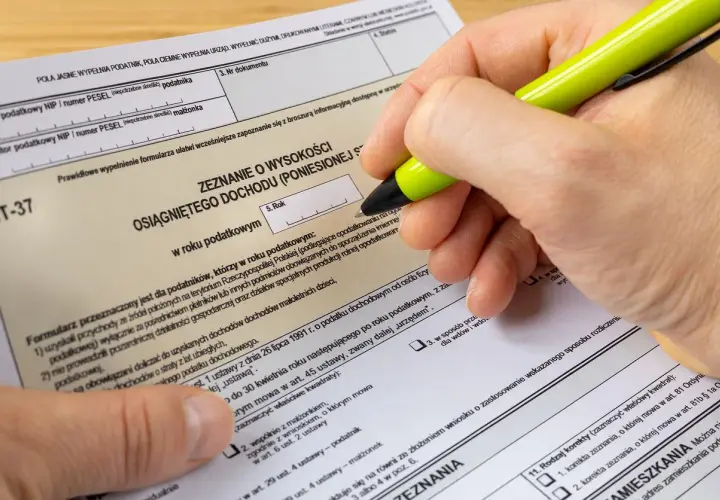 Dłoń z zielonym długopisem wypełnia formularz PIT-37.