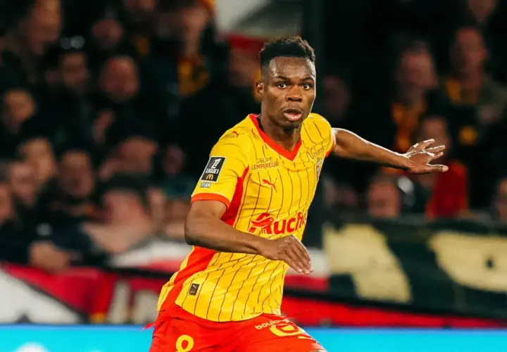 Piłkarz RC Lens w żółto-czerwonej koszulce biegnie po boisku, gotowy do akcji przeciwko Stade Rennais.