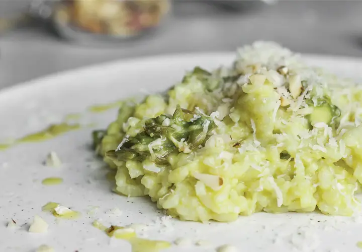Kremowe risotto ze szparagami, posypane parmezanem i migdałami, na białym talerzu.