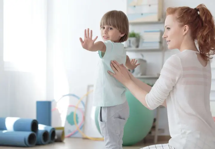 Ein Kind mit Skoliose erhält osteopathische Behandlung. Eine Therapeutin legt sanft die Hände auf den Rücken des Jungen, der sich leicht wegdreht.