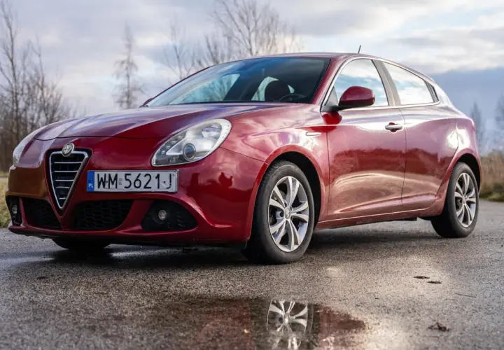 Czerwone Alfa Romeo Giulietta na mokrej drodze. Wiele osób szuka alfa romeo giulietta opinie przed zakupem.