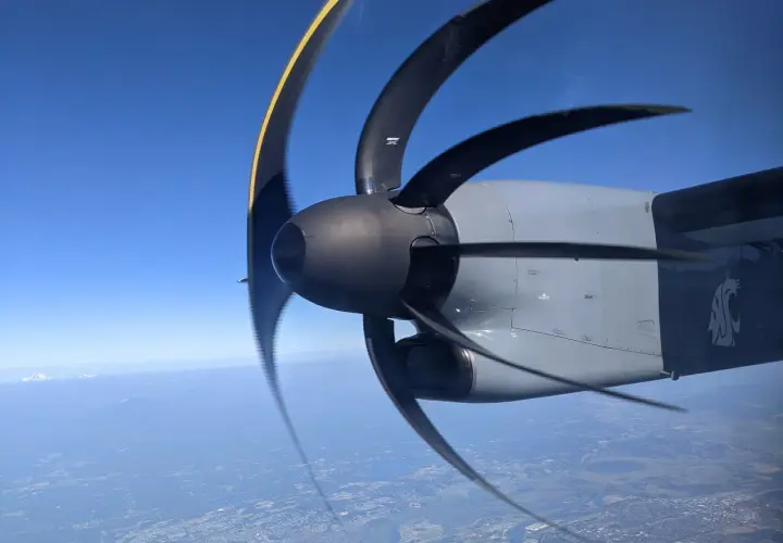 Wirujący silnik samolotu z widocznym efektem rolling shutter. W tle błękitne niebo i krajobraz z lotu ptaka.