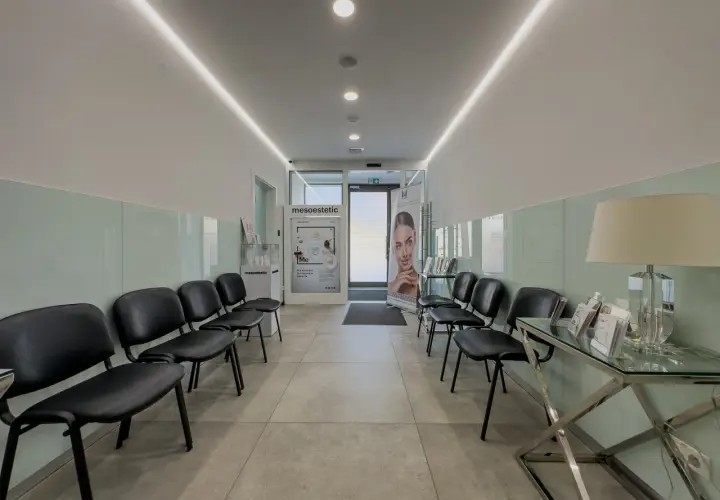 Nowoczesna poczekalnia z czarnymi krzesłami, podświetlanym sufitem i banerem reklamowym.