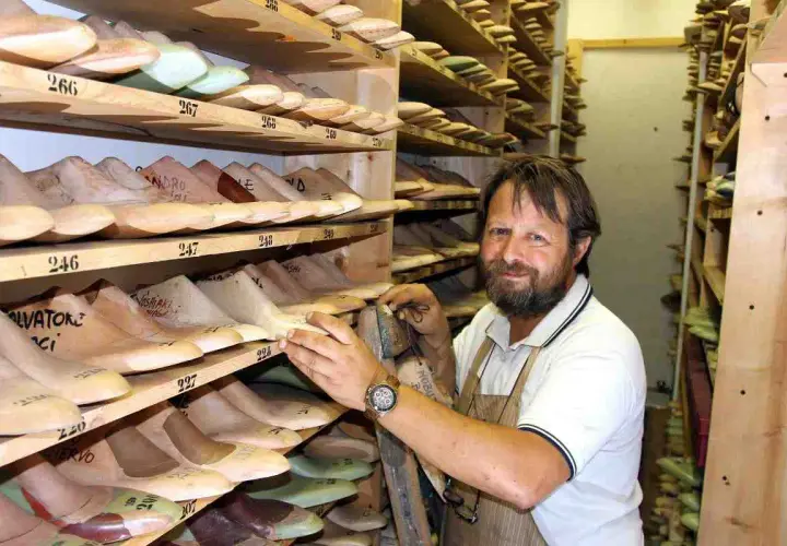 Un calzolaio sorridente in bottega, circondato da forme di legno per scarpe. Sembra Daniel Day Lewis, immerso nel suo mestiere.