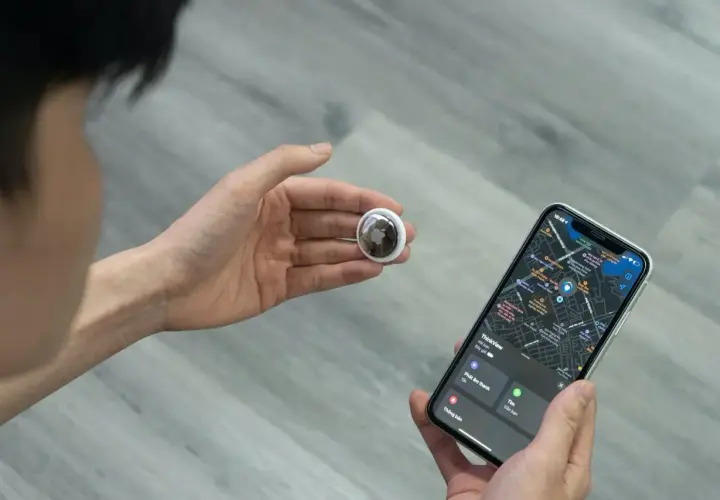 Osoba trzymająca w dłoni lokalizator AirTag i iPhone'a z mapą. AirTag co to? To małe urządzenie do śledzenia zgubionych przedmiotów.