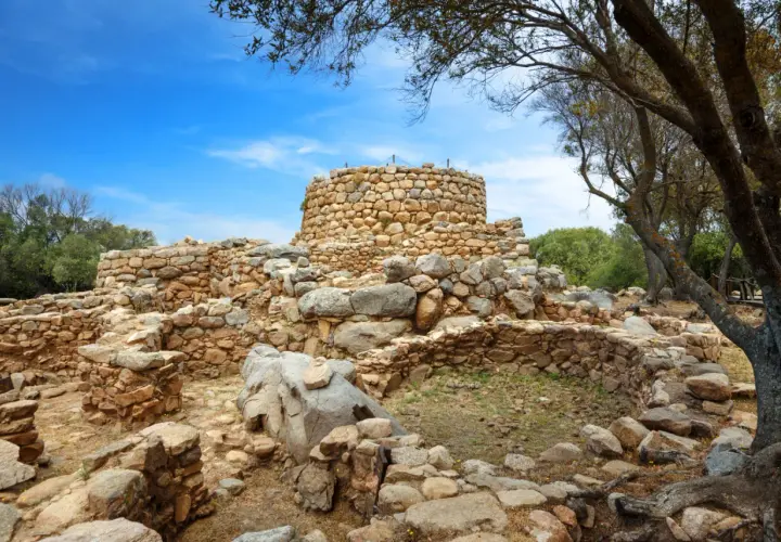 Rovine di un nuraghe in pietra sotto un cielo azzurro. Un mistero su chi ha costruito i nuraghi.