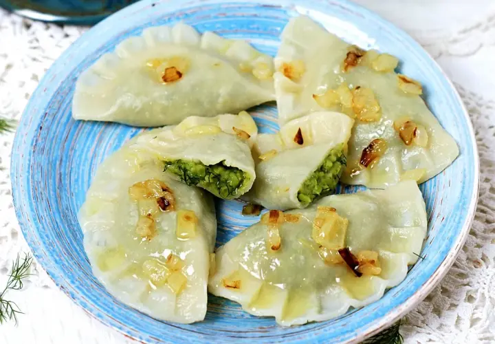 Pyszne pierogi z bobem, polane skwarkami z cebulki, na niebieskim talerzu.