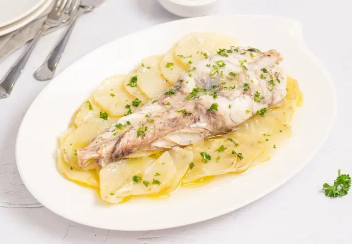 Rape al horno servido sobre patatas laminadas y espolvoreado con perejil fresco.