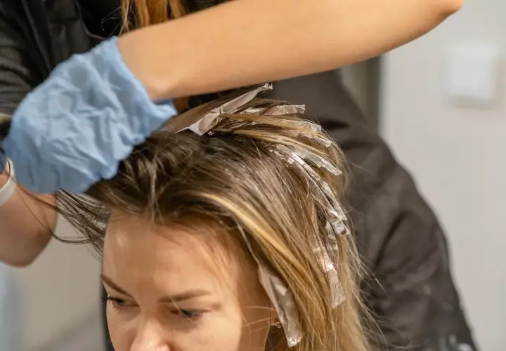 Manos enguantadas aplican mechas con papel de aluminio para un look face framing.