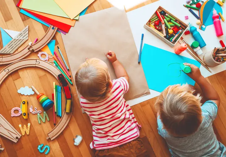 Dos niños pequeños disfrutan de actividades para niños de un año en guardería: pintan y juegan con un tren de madera.