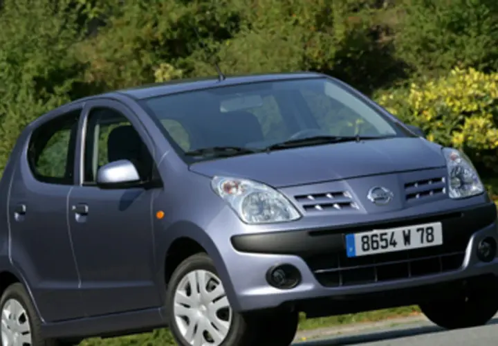 Niebieski Nissan Pixo z tablicą rejestracyjną 8654 W 78 zaparkowany na tle zieleni.