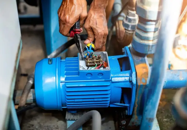 Manos trabajando en la caja de conexiones de un motor azul, revisando el cableado. El **vac significado** es crucial para el funcionamiento de esta bomba.