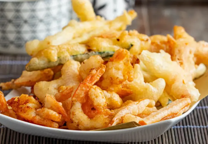 Un piatto invitante di gamberi in tempura dorati e croccanti, accompagnati da verdure fritte.