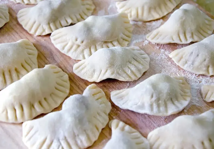Surowe pierogi z kaszą gryczaną ułożone na drewnianej desce, posypane mąką.