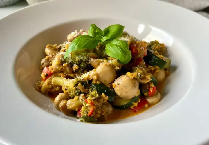 Pyszne kaszotto z warzywami: brokuły, cukinia, pieczarki i pomidorki, posypane parmezanem i udekorowane bazylią.