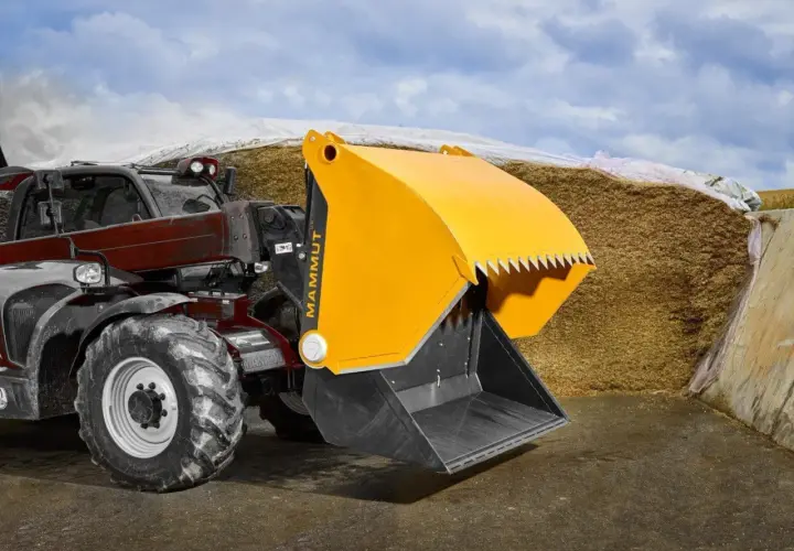 Ein Teleskoplader mit gelber Schaufel steht vor einem großen Silo in der Landwirtschaft.