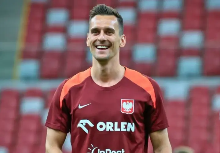 Uśmiechnięty piłkarz w koszulce reprezentacji Polski, mimo że jego **milik kontuzja** mogła go martwić, wygląda na zrelaksowanego.