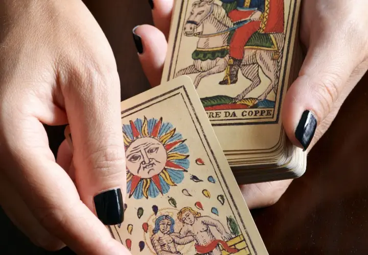 Dłonie trzymają karty tarota, w tym Słońce i rycerza na koniu. Sprawdź, czy tarot online, który się sprawdza, pomoże Ci odkryć przyszłość.