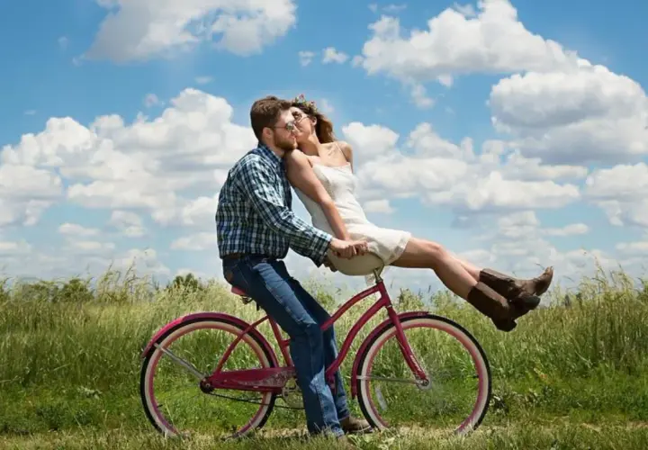 Coppia su bici rosa, lei seduta davanti a lui, baci appassionati sotto un cielo azzurro. Ecco perchè ci si innamora.