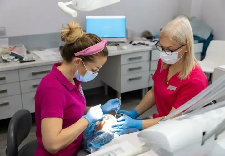 Dwie dentystki w maskach pracują przy pacjencie. Zastanawiasz się, ile schodzi znieczulenie od dentysty?
