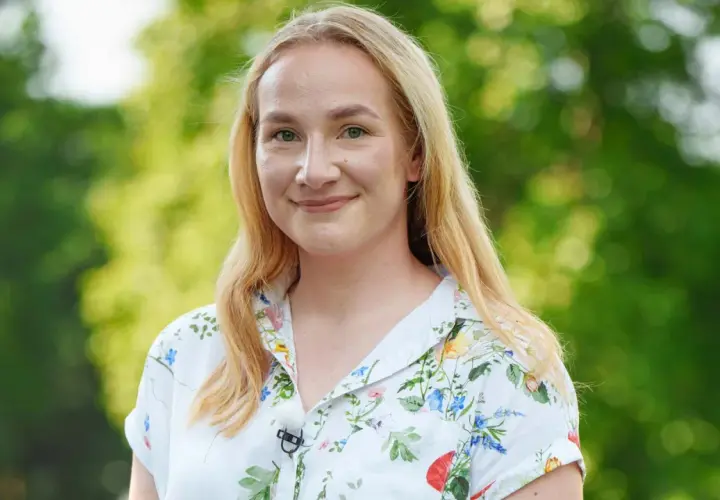 Uśmiechnięta Klaudia, uczestniczka "Rolnik szuka żony", w kwiecistej koszuli na tle zieleni.