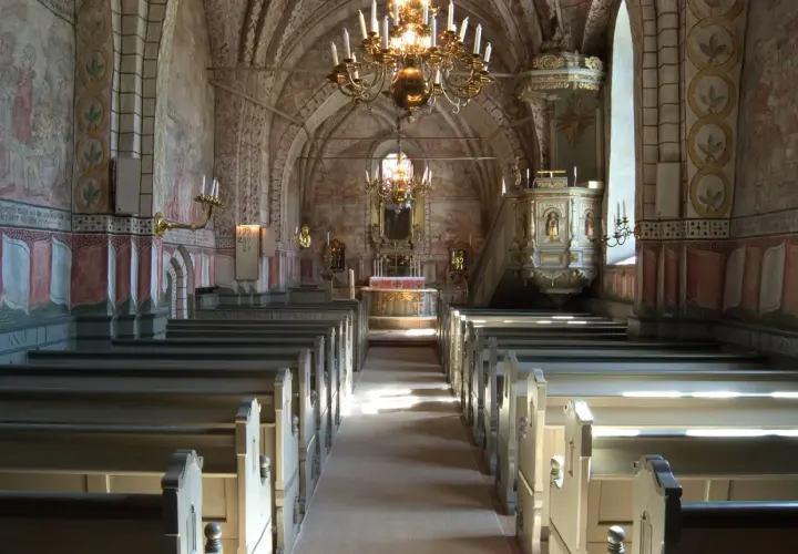 Interiör av en kyrka med bänkar, altare och en predikstol. Väggmålningar och en stor ljuskrona skapar en historisk atmosfär. En av många vackra kyrkor i Stockholm.