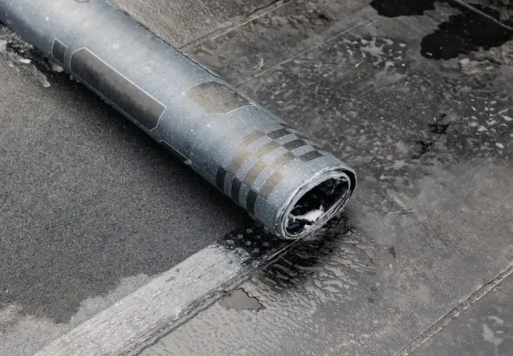 Zrolowana papa na zimno, z charakterystycznym wzorem, leży na mokrej, ciemnej powierzchni.