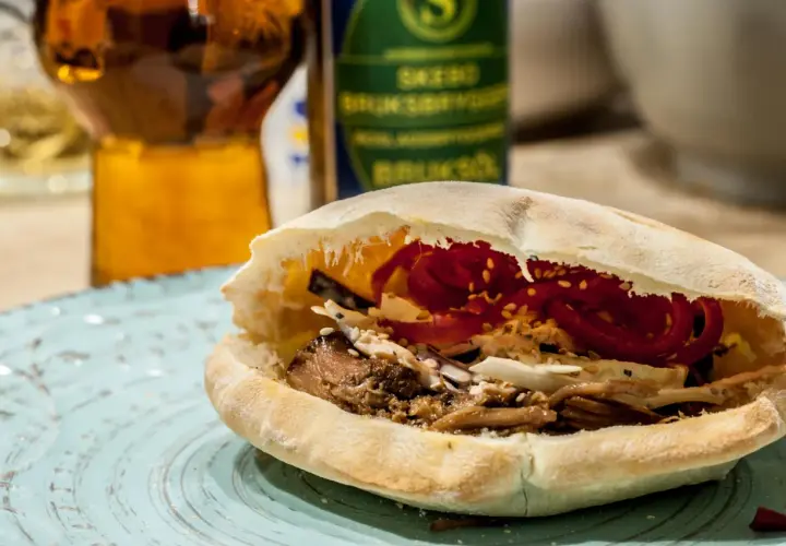 En saftig pulled pork karre-macka i pitabröd, fylld med krispig kål och rödlök. En öl i bakgrunden.