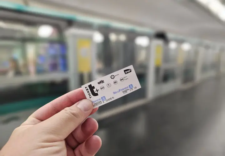 Dłoń trzyma bilet metra paryskiego na tle pociągu.