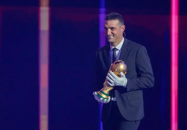 Uśmiechnięty trener Argentyny, Lionel Scaloni, trzyma Puchar Świata w złotych rękawiczkach.