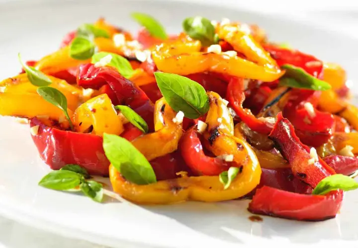 Peperoni al forno colorati, dolci e succosi, guarniti con basilico fresco e aglio. Un contorno estivo perfetto.