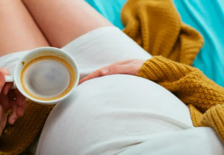 Una donna incinta si gode un caffè, con la mano che accarezza il pancione. Un momento di relax e dolce attesa.