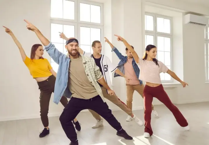 Grupa młodych ludzi wykonuje energiczne ruchy taneczne w jasnej sali.