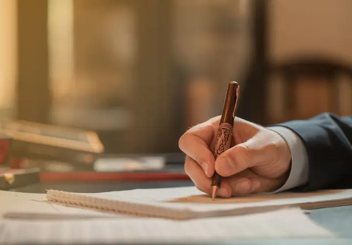 Dłoń pisze piórem ozdobnym na papierze. Zapewne to wniosek o stwierdzenie nabycia spadku, który wymaga staranności.