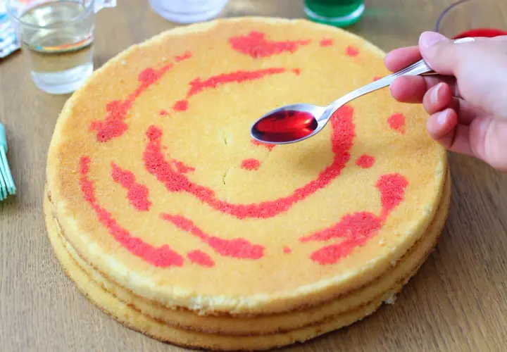 Un cucchiaino di sciroppo rosso viene versato su un pan di spagna a strati, creando un disegno.