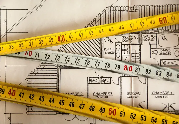 Cintas métricas sobre planos de construcción, ilustrando la diferencia de metros entre registro de propiedad y catastro.