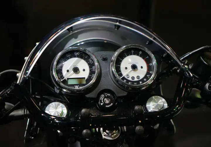 Klasyczny przebieg motocykla: prędkościomierz i obrotomierz w chromowanych obudowach, podświetlane kontrolki i kluczyk zapłonu.