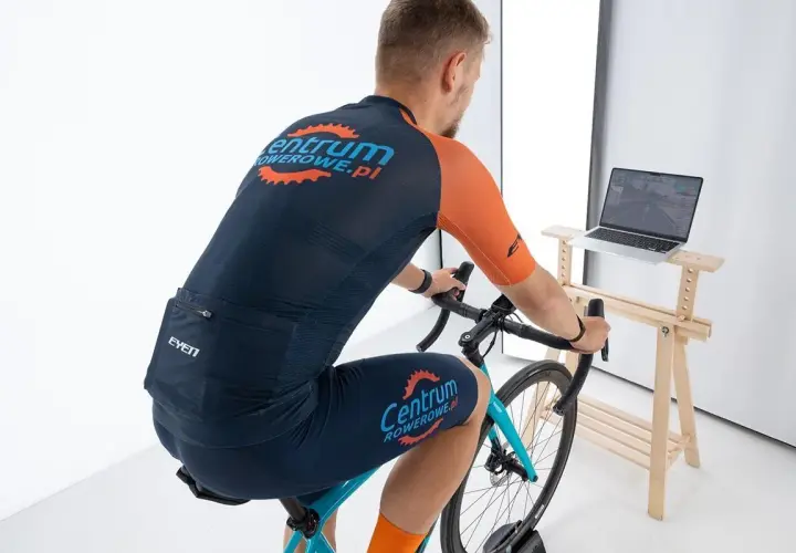 Mężczyzna na rowerze stacjonarnym, ćwiczący cardio. Na ekranie laptopa widać wirtualną trasę kolarską.