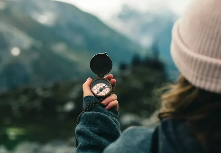 A person in a pink beanie holds a compass, navigating a misty mountain landscape. This symbolizes the journey of transition coaching.
