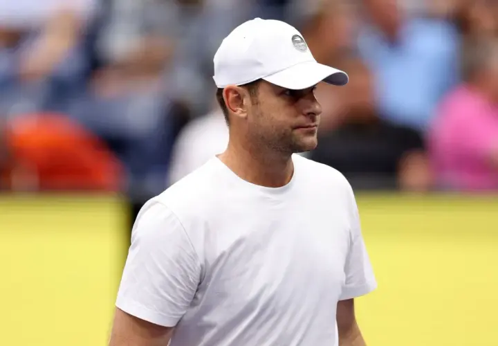 Andy Roddick w białej czapce z logo US Open i białej koszulce, zapatrzony w dal.
