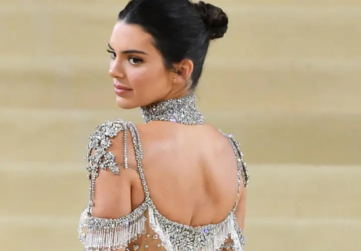 Mujer con un elegante moño recogido, luciendo un vestido de pedrería y un collar brillante.
