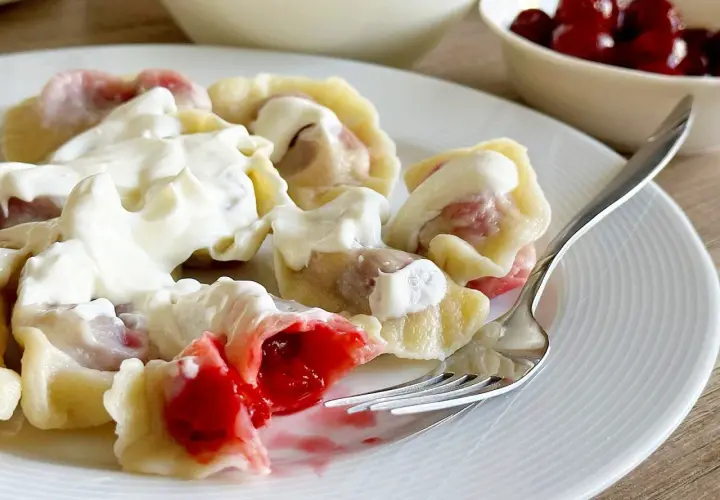 Pyszne pierogi z wiśniami, polane gęstą śmietaną, kuszą soczystym nadzieniem. Idealne na deser lub słodki obiad.