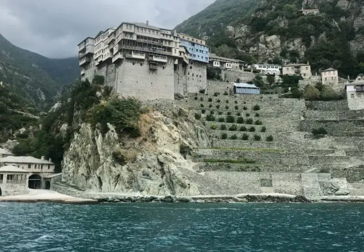 Monastyr na Athos, zbudowany na skalistym zboczu, z tarasowymi ogrodami i widokiem na morze.