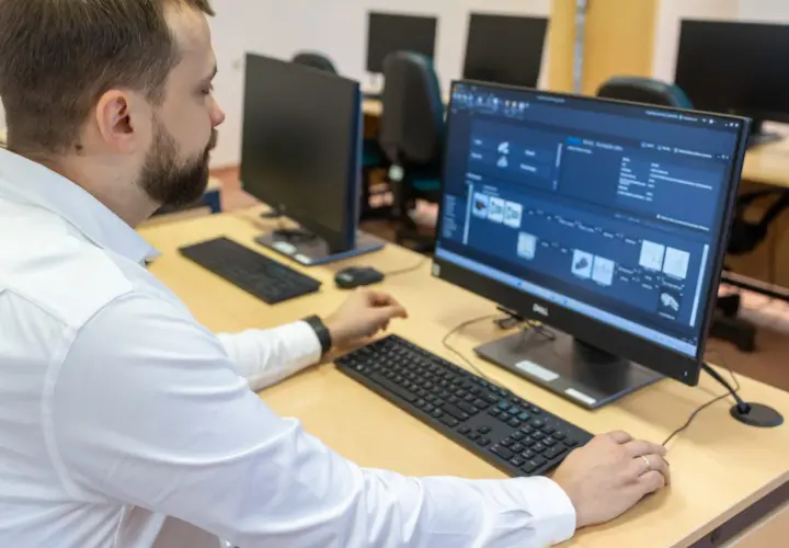 Mężczyzna w białej koszuli pracuje przy komputerze, analizując dane produkcyjne. To przykład nowoczesnego zarządzania i inżynierii produkcji.
