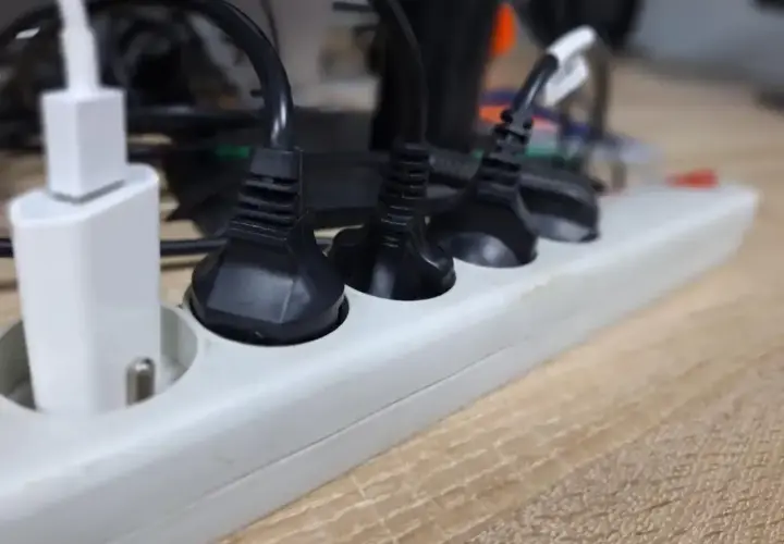 Wieloportowa listwa zasilająca z wieloma wtyczkami, w tym białą ładowarką USB, pokazuje potrzebę przedłużania przewodów elektrycznych.