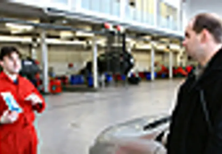 Mechanik w czerwonym kombinezonie omawia z klientem kwestie związane z ekologicznym paliwem, takim jak biodiesel, w warsztacie samochodowym.
