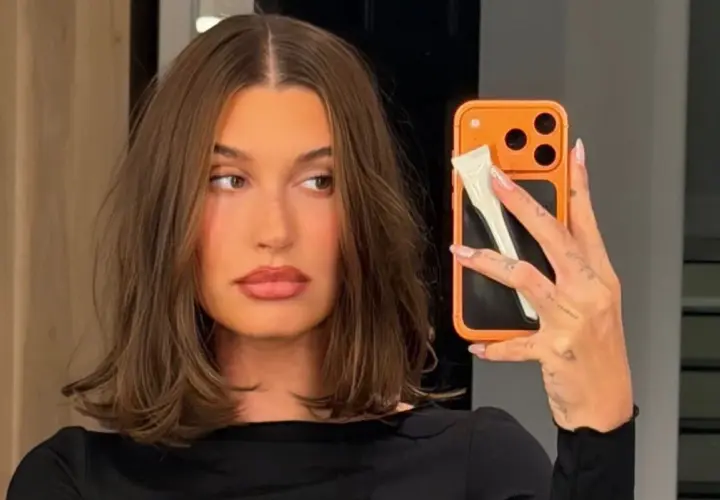 En kvinna med fina hårfrisyrer tar en selfie med sin orangea mobil.