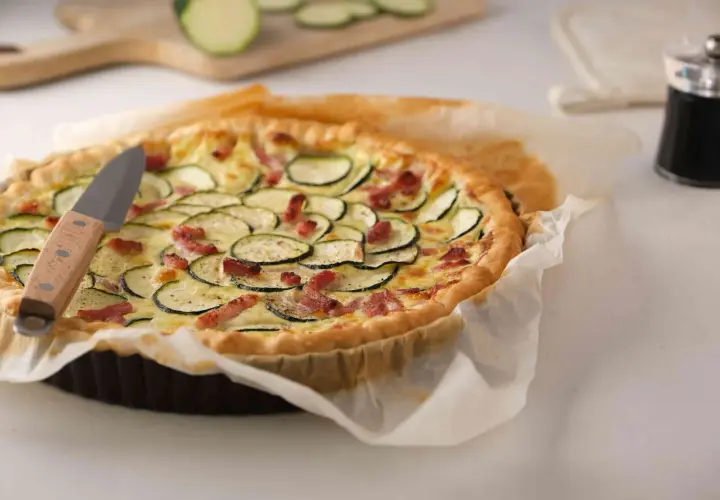 Une délicieuse quiche courgette lardon dorée, garnie de rondelles de courgettes et de lardons croustillants, prête à être dégustée.